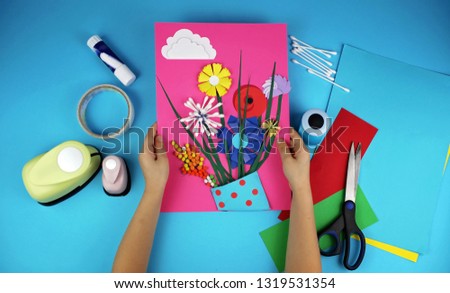 Cute 5-6 years old girl making spring DIY flowers with colored paper for her mom in Mothers Day, decorative punchers to create fun and easy with children, concept for kindergarten, top view image