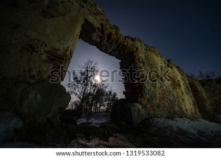 The wall of an old building with a hole in the winter. Entrance to an abandoned house. Ruins of an ancient castle at night.
