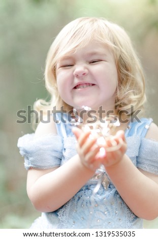 Cute little blonde girl in a blue princess dress is holding fairy lights outside on a sunny day