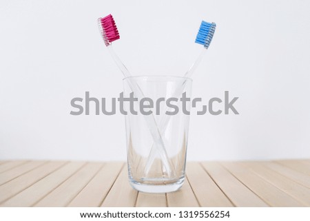 A glass with two plastic toothbrushes on white and wooden background