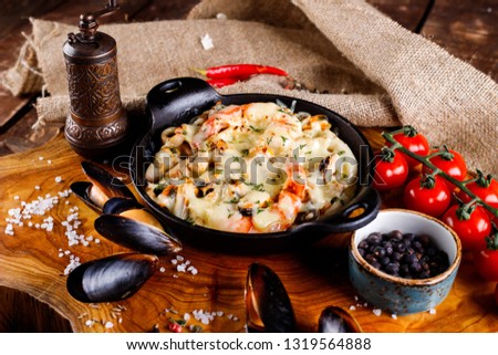 Delicious seafood in white sauce on a metal black plate, a number of products for cooking, tomatoes, champignons.