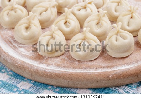 Homemade uncooked pelmeni on a wooden board on the checkered tablecloth.