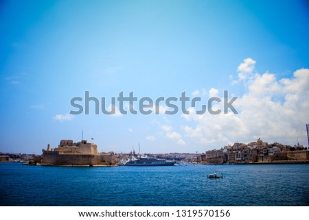 
the picture shows a huge cruiser that is anchored on the coast of the city of Valletta, located in Malta. The picture was taken from the boat from the boat. On the left and right are old buildings