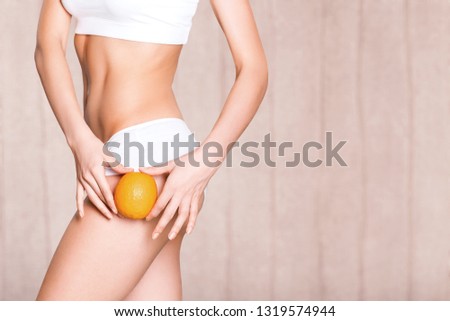 Female slender body in sport underwear holding orange on sea background
