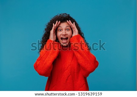 Indoor shot of surpised excited woman doesn`t believe her success, keeps hands on head, stares at camera, says omg or wow. Pleasant surprised female looks amazed Royalty-Free Stock Photo #1319639159