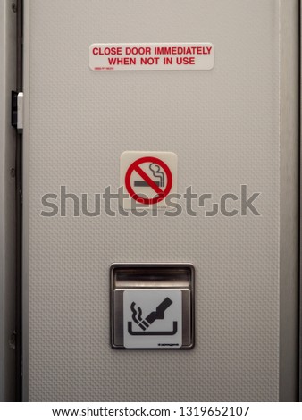 The interior of an airplane bathroom door with an ashtray, a no smoking sign, and a "close door immediately when not in use" sign. The FAA requires ashtrays inside and outside airplane lavatories