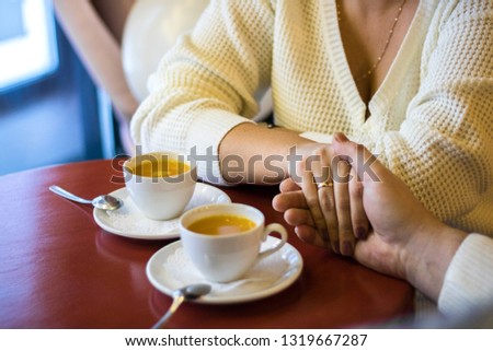 Couple hold hands in cafe, drinking tea, close up of lovers arms on background of wooden table with two white cups with tea on it. date in cafe