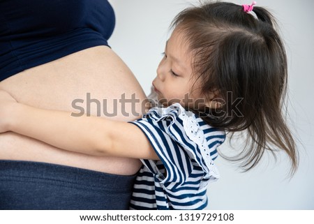 Little girl kissing her sister in pregnant mother's belly