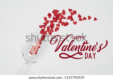 top view of wine glass and small paper cut hearts on white background with "Happy valentines day" lettering 