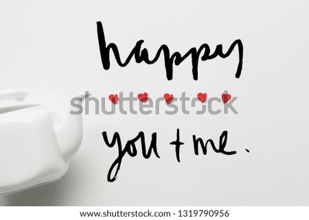 top view of tea pot and red paper cut hearts on white background with love lettering 