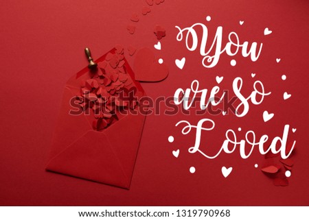 top view of paper cut hearts and opened envelope on red background with "you are so loved" lettering