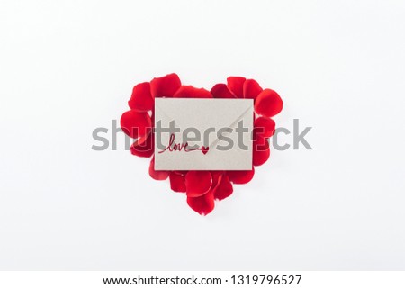 top view of envelope with "love" lettering and heart made of red rose petals isolated on white, st valentines day concept