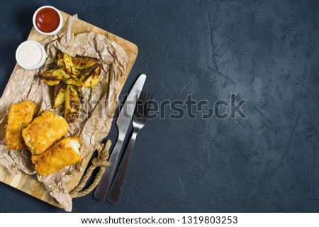 English traditional fish and chips on a wooden chopping Board. Dark background, top view, space for text