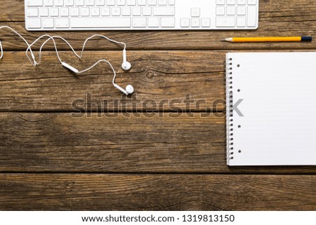 keyboard, note pad, earphones on rustic wooden table background, top view