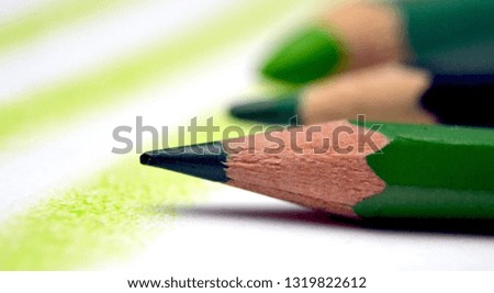 Three green pencils of different shades on the background of a white sheet of paper with green lines drawn.