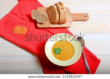 Red lentil soup on the plate on wooden white table red napkin spoon and bread still life food 