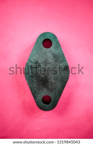close-up of a thick metal piece with two holes, similar to a diamond and located on a pink glossy background