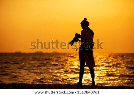 Silhouette of  woman  professional photographer standing on the beach shooting photo ,female  taking pictures with sunset,Lifestyle relaxation travel concept