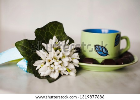A cup of tea with pieces of black chocolate and a bunch of snowdrops on the table.