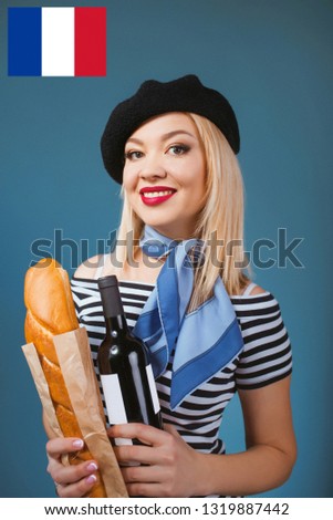 portrait of beautiful blonde french woman in beret, scarf, back and white shirt, with bottle of wine and bread baguette in her arms with French flag on background