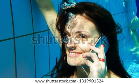 An attractive woman talking on a cell phone under water in a swimming pool