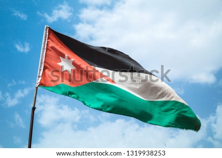 Flag of Jordan waving on wind over blue cloudy sky background