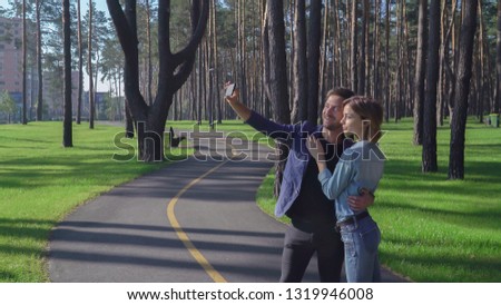 Young happy couple taking self portrait photo in the park. Dating pair take selfie outdoors. Guy holding smartphone takes a photograph himself and pretty girl with beautiful smile.