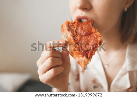 Girl in a pajama bites a delicious pizza, close-up and enjoyment. Woman eating pizza, cropped photo.Background. Copyspace