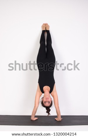 Beautiful girl in a tracksuit on a white background. Performs asana stance on the head in yoga. Woman doing yoga power exercises.