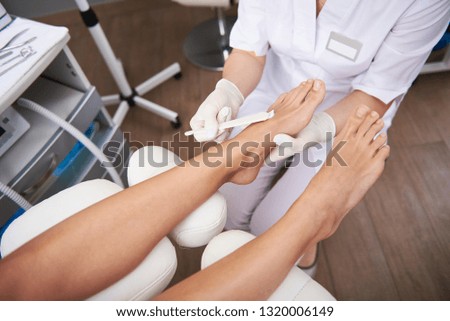 Close up top view picture of female hands in white sterile gloves putting restorative and moisturizing lotion on woman leg
