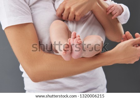 Cropped and close up photo of mama with baby on hands standing isolated on gray background. In center of image baby foot
