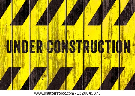 Under construction warning sign text with yellow black stripes painted on wood wall plank texture wide background. Concept do not enter the area, caution, danger, construction site.