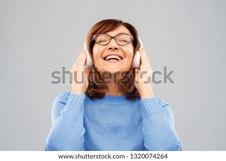 technology and old people concept - smiling senior woman in glasses and headphones listening to music over grey background