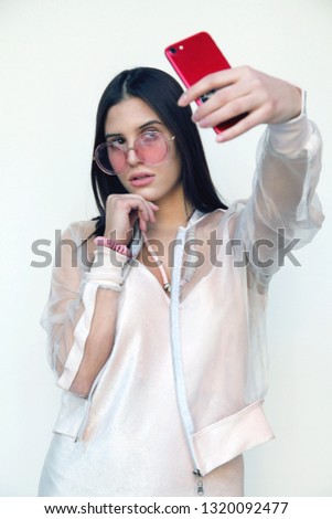 Beautiful girl pretty dark hair caucasian taking selfie phone photograph white background in pink sunglasses jewelry gorgeous style teenage fashion attractive young look bold selfportrait popular    