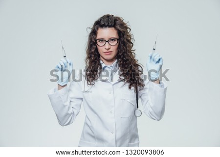 Doctor of medical staff in white uniform holding syringes in his hands on a gray background and looking directly at the camera. Health and Medical Aid, Concept. Portrait of a nurse.