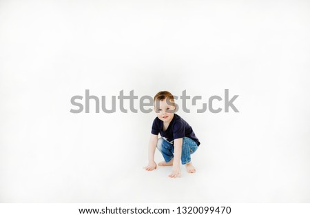 Emotional portrait of a happy and mischievous little boy looking with a smile at the camera while sitting on the white floor in the playroom. Copy space. Happy childhood. Lifestyle. Positive energy