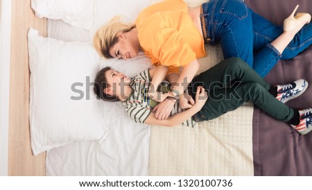 Mother with son having fun, mom and her teenager son lying on bed, mother with child relaxing, modern mom with kid at home, top view