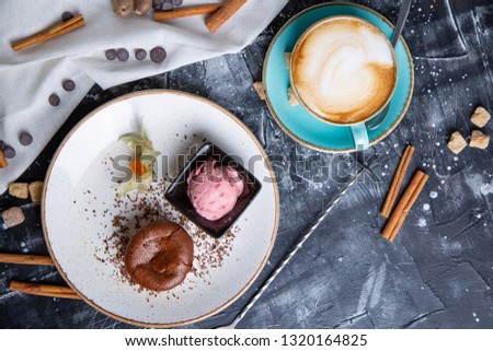 Chocolate lava cake Molten with ice cream on plate and cappuccino. Balls of ice cream in cup . Dark black background.