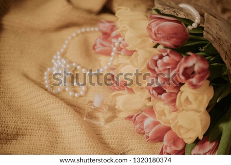 Toned picture of pink and yellow tulips bouquet lying on a yellow knitted fabric with pearl beads and small bottle of perfume stands nearby shallow depth of field 
