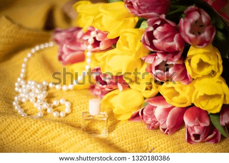 Toned picture of pink and yellow tulips bouquet lying on a yellow knitted fabric with pearl beads and small bottle of perfume stands nearby shallow depth of field 