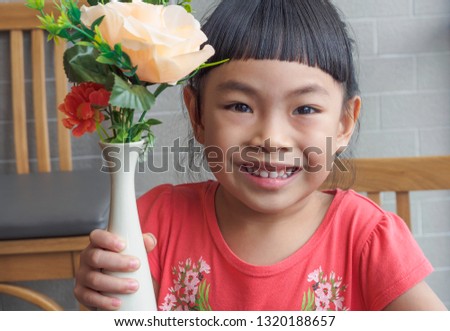 Portrait of little girl holding flower vase. Big smiley face and looking at camera