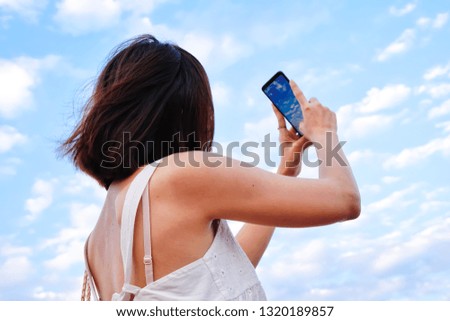 young woman wearing white dress shows burn skin from sunlight use smartphones to take pictures of the blue sky and white cloud, ant angle view