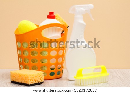 Plastic bottles of dishwashing liquid, glass and tile cleaner, brush, basket with sponges on beige background. Washing and cleaning concept.