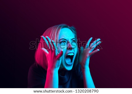 Screaming, hate, rage. Crying emotional angry woman screaming on neon studio background. Emotional, young face. Female half-length portrait. Human emotions, facial expression concept. Trendy colors