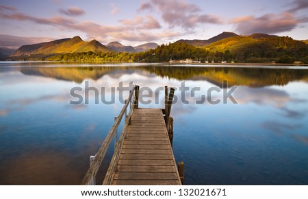 An old jetty on the still water of Derwent Water in Cumbria stretches towards the hills in the distance. Royalty-Free Stock Photo #132021671