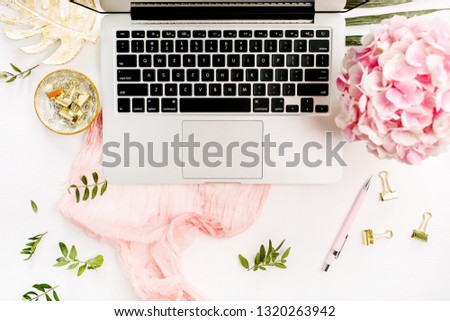 Woman home office desk with laptop, pink hydrangea flowers bouquet, pastel blanket, monstera leaf plate and accessories on white background. Flat lay, top view rose gold workspace.