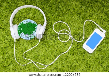 Give peace a music! White headphones and ball made of thread with map on it, on the green carpet.