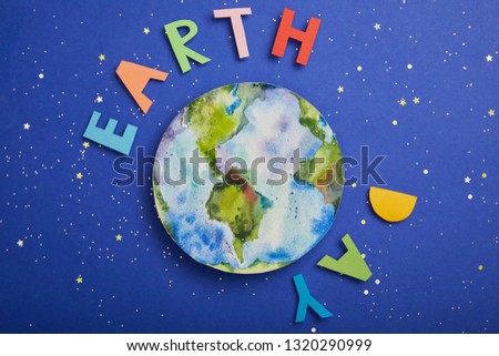 top view of colorful paper letters and planet picture on violet background with stars, earth day concept