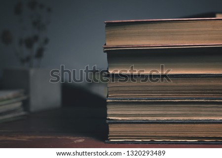 a stack of four old vintage books on a wooden table and a dry flower on the background