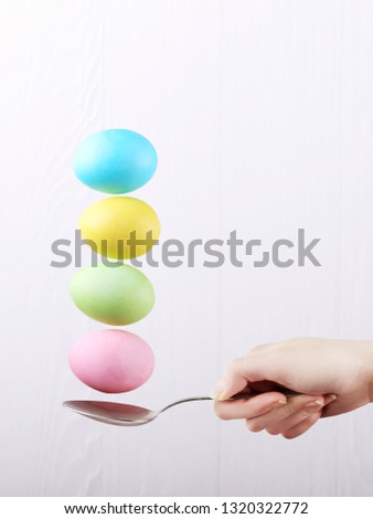 Female hand holds a spoon on which multi-colored eggs are balanced, on white background. Unusual design, Easter concept, copy space.